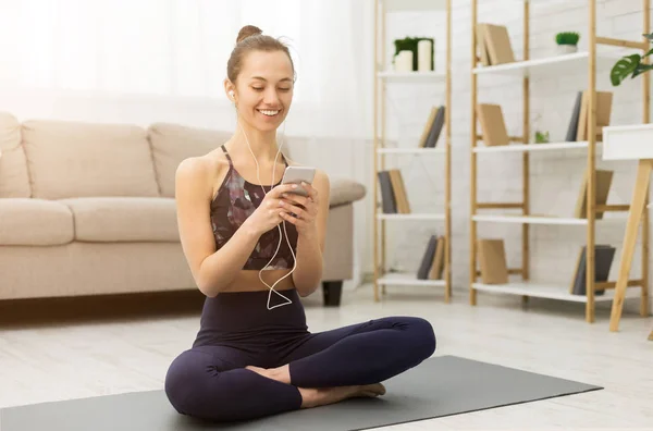 Woman after practicing yoga, relaxing on mat with smartphone — Stock Photo, Image