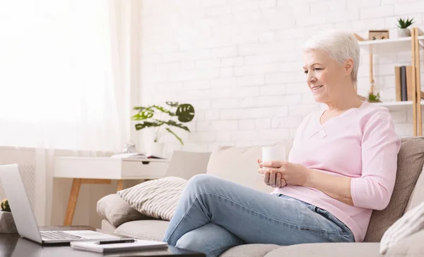 Starsza kobieta siedzi na kanapie i oglądanie filmów online — Zdjęcie stockowe