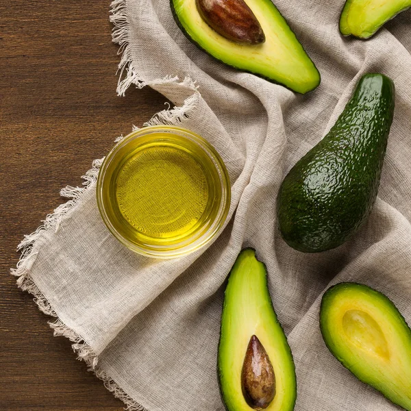 Geschnittene und ganze Avocados und eine Schüssel Öl auf dem Tisch — Stockfoto