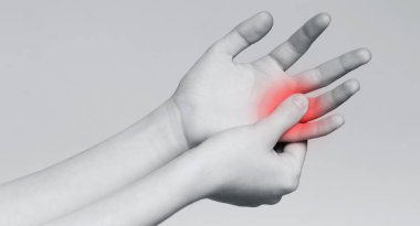 Genç bir kadın acılı parmağına masaj yapıyor, tek renkli.