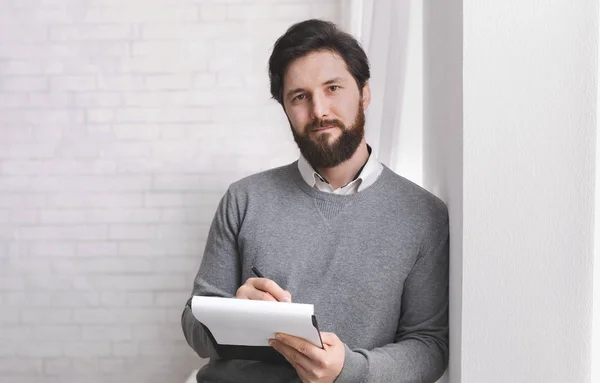 Friendly psychologist standing with clipboard, leaning at wall — Stock Photo, Image