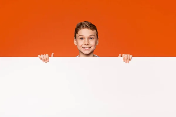 Aranyos mosolygós fiú keresi ki a fehér üres plakát — Stock Fotó