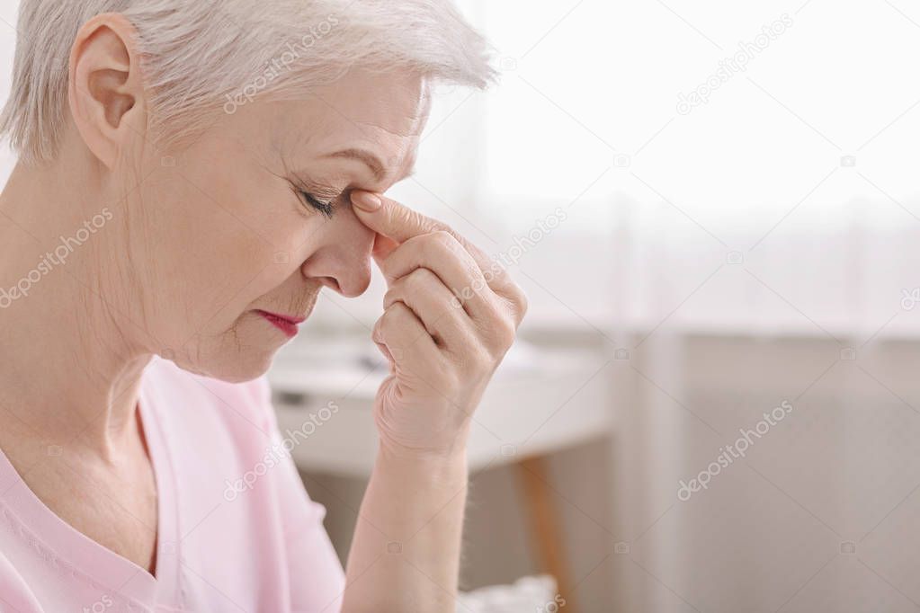 Fatigued senior woman massaging nose bridge, feeling eye strain