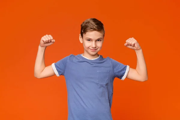 Söt pojke visar biceps på Orange bakgrund — Stockfoto