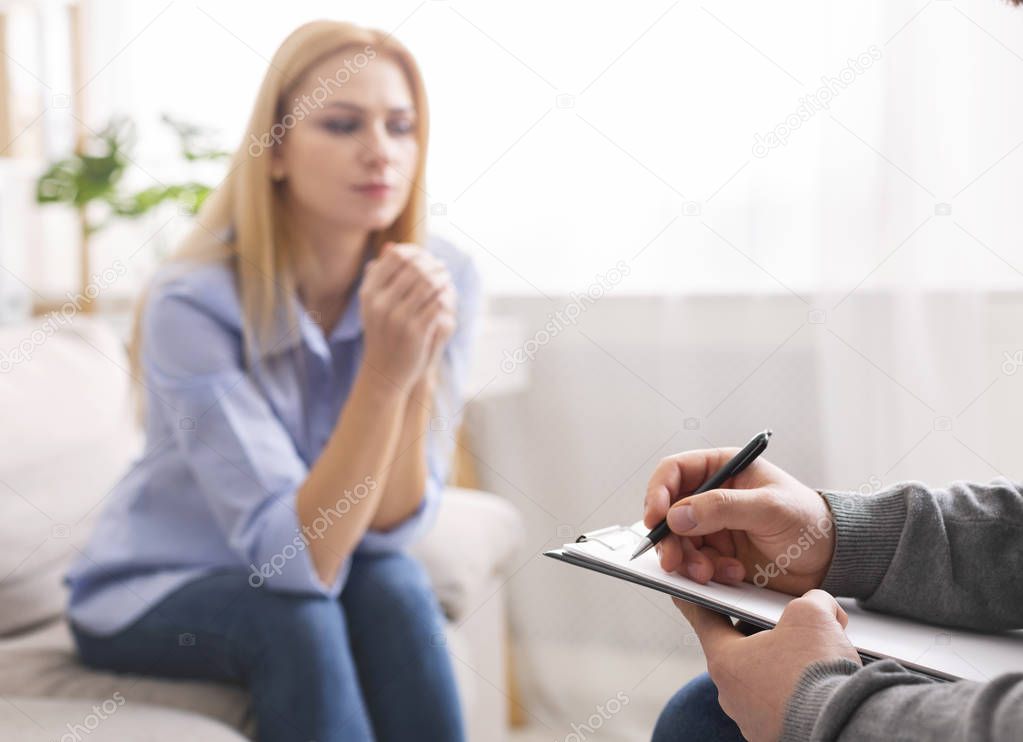 Therapist taking notes, listening to sad woman at personal consultation