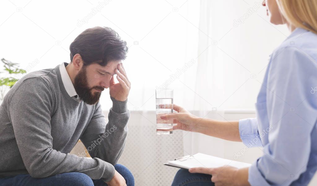 Psychoanalyst offering glass of water to depressed male patient
