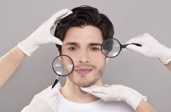 Face of young handsome man with beauticians hands and magnifiers