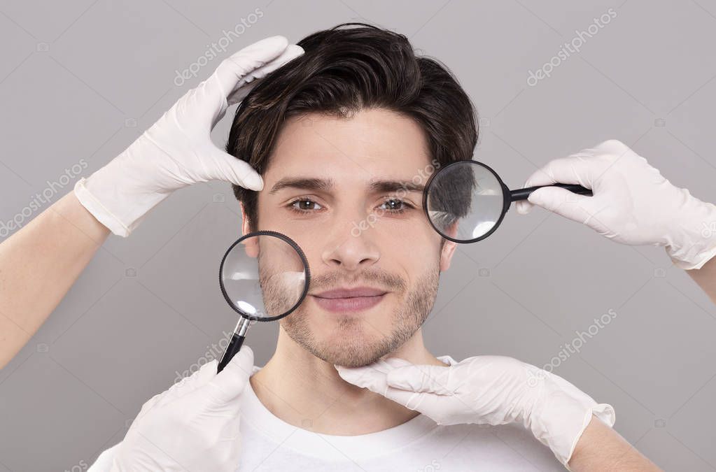Face of young handsome man with beauticians hands and magnifiers