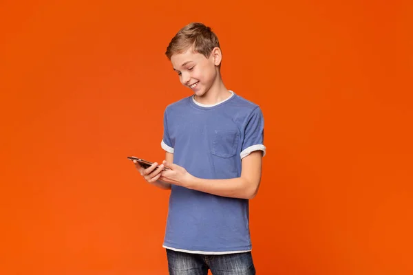 Цікавий хлопчик-підліток використовує смартфон на помаранчевому фоні — стокове фото