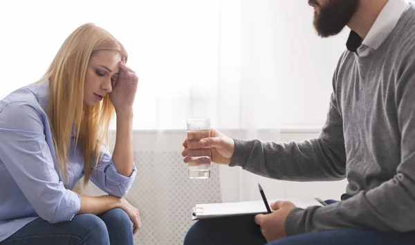 Psicoterapeuta que ofrece un vaso de agua para molestar a la paciente llorando —  Fotos de Stock