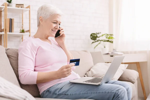 Старшая женщина делает покупки онлайн и разговаривает по телефону — стоковое фото