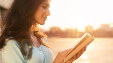 Dışarıda kitap okumak. Gün batımında şehirde yürüyen genç kadın