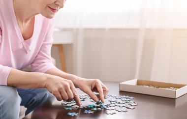 Evde ahşap masada yapboz oynayan yaşlı kadın