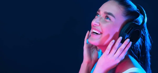 Девушка слушает музыку в наушниках, освещенную неоновым светом — стоковое фото