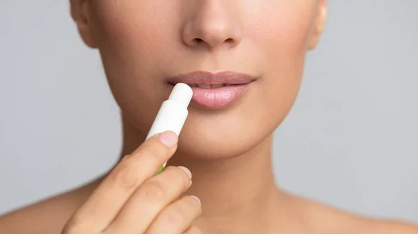 Girl applying hygienic lip balm on grey background — Stock Photo, Image