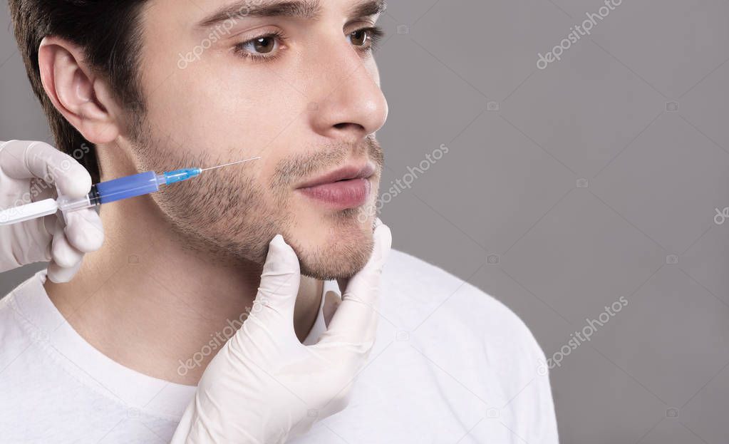 Confident young man having filler injection in his cheek-bone