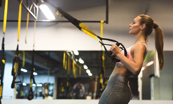 Mujer joven realizando entrenamiento TRX en gimnasio, espacio para copiar — Foto de Stock