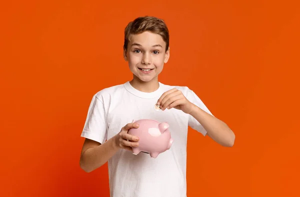 Menino colocando dinheiro de bolso no banco porquinho — Fotografia de Stock