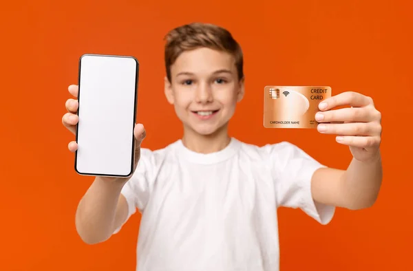 Wesoły chłopiec trzyma pusty smartfon i kartę kredytową — Zdjęcie stockowe