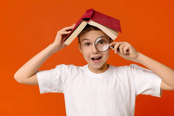 Netter schlauer Junge mit Lupe in der Hand versteckt sich unter Buch — Stockfoto