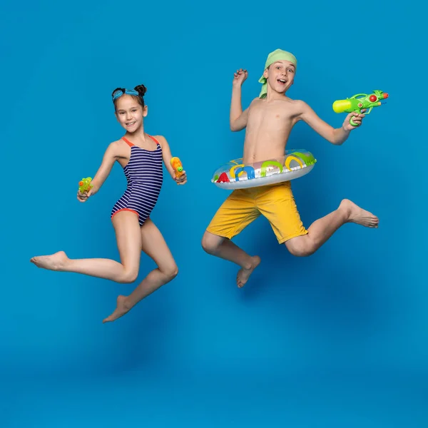 Счастливые брат и сестра в купальниках прыгают с водяными пистолетами — стоковое фото