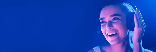 Kobieta słuchanie muzyki w słuchawkach oświetlonych przez niebieskie światło — Zdjęcie stockowe