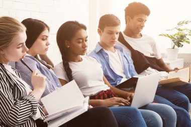 Dizüstü bilgisayar ve kitaplarla sınavlara hazırlanan çok ırklı öğrenciler