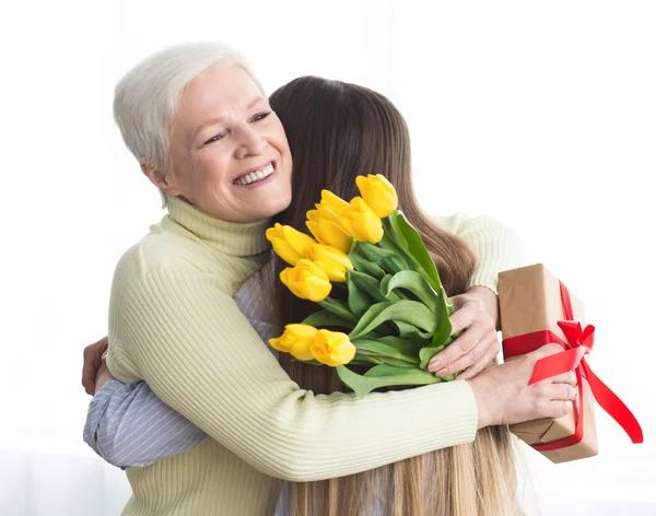 Filha dando flores e presente para sua mãe — Fotografia de Stock