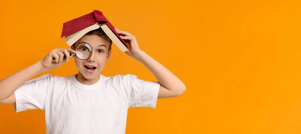 Chłopiec ukrywający się pod książką i patrząc przez lupę — Zdjęcie stockowe