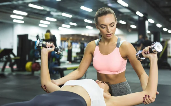 Entrenador ayudando a la mujer en el gimnasio, dando entrenamiento de levantamiento de pesas —  Fotos de Stock