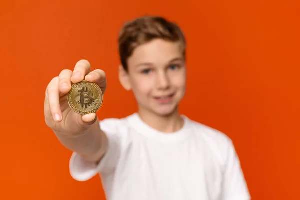 Ragazzo allegro in possesso di bitcoin d'oro, sfondo arancio studio — Foto Stock