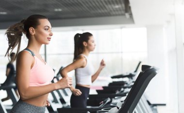 Fit kızlar koşu bandı üzerinde kardiyo eğitimi yapıyor