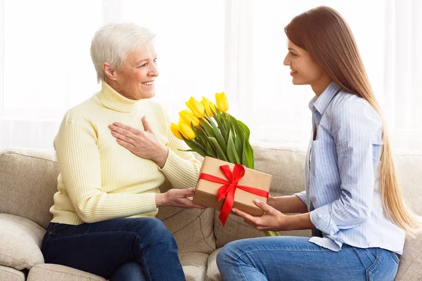 Daughter giving tulips and gift box to her mother