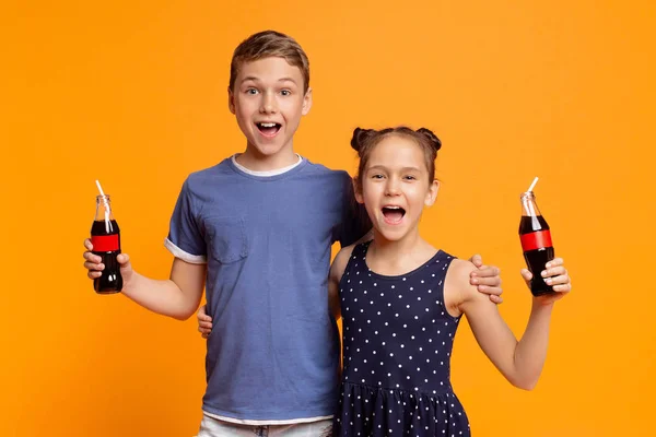 Emocionado niño y niña sosteniendo botellas con bebida fresca — Foto de Stock