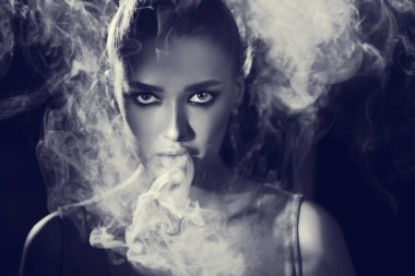 Woman Smoking Vape And Exhaling Smoke In Studio clipart