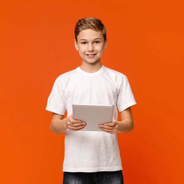 Teenager-Junge mit digitalem Tablet auf orangefarbenem Studiohintergrund — Stockfoto