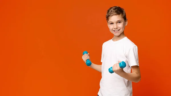 欢快的男孩用哑铃锻炼，橙色背景 — 图库照片