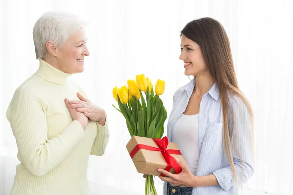 Woman giving tulips and gift box to her mature mother
