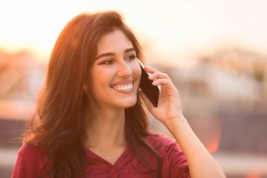 Mutlu öğrenci akıllı telefonda konuşuyor, gün batımında yürüyor