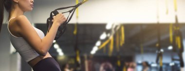 Spor salonunda süspansiyon eğitmeniyle egzersiz yapan bir kadın.