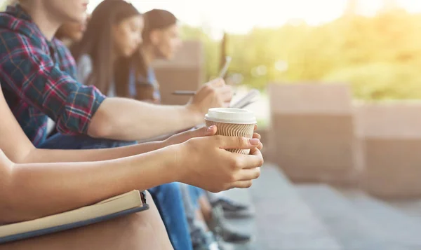 Grupo de adolescentes sentados al aire libre, chica sosteniendo una taza para llevar — Foto de Stock