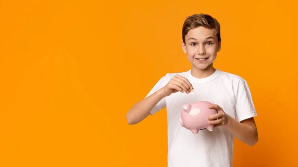 Sorrindo menino colocando dinheiro no banco porquinho — Fotografia de Stock