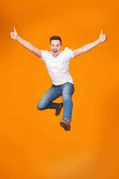 Захоплений молодий чоловік стрибає, святкуючи успіх над фоном студії — стокове фото