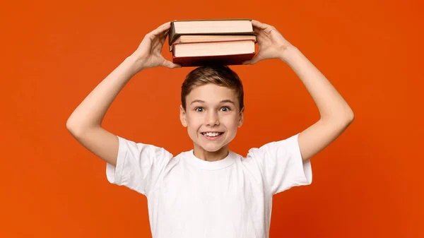 Positiv skolpojke innehar högen av böcker på huvudet — Stockfoto