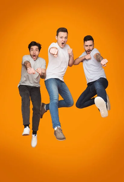 Tres hombres emocionados saltando juntos sobre fondo amarillo —  Fotos de Stock