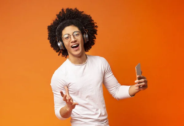 Bushy millennial guy chanter avec téléphone sur fond orange — Photo