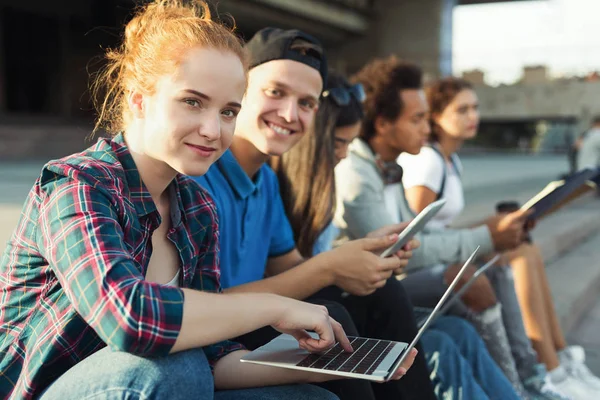 Söt rödhårig flicka med hjälp av laptop, studera med hennes tonårs vänner — Stockfoto