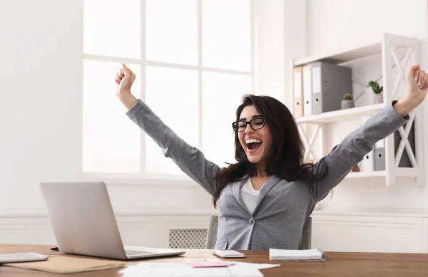 Imprenditrice eccitata che celebra il successo con mani alzate sul posto di lavoro — Foto Stock