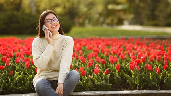 Chica feliz hablando por teléfono cerca de Tulipanes rojos — Foto de Stock
