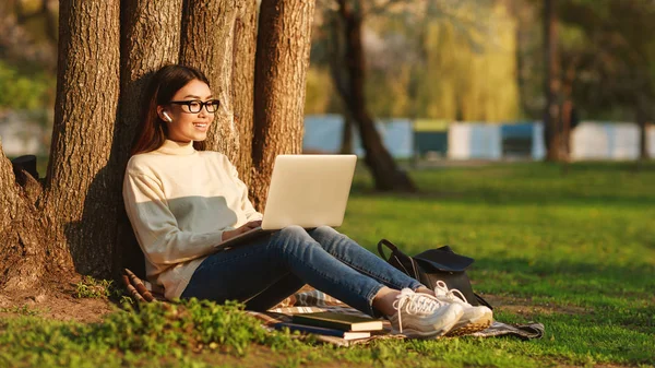 Asijská dívka použití přenosného počítače pod stromem na universitním kampusu — Stock fotografie